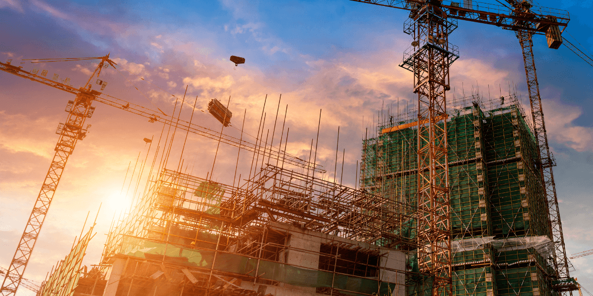 Construction site at sunset with cranes and scaffolding against a colorful sky