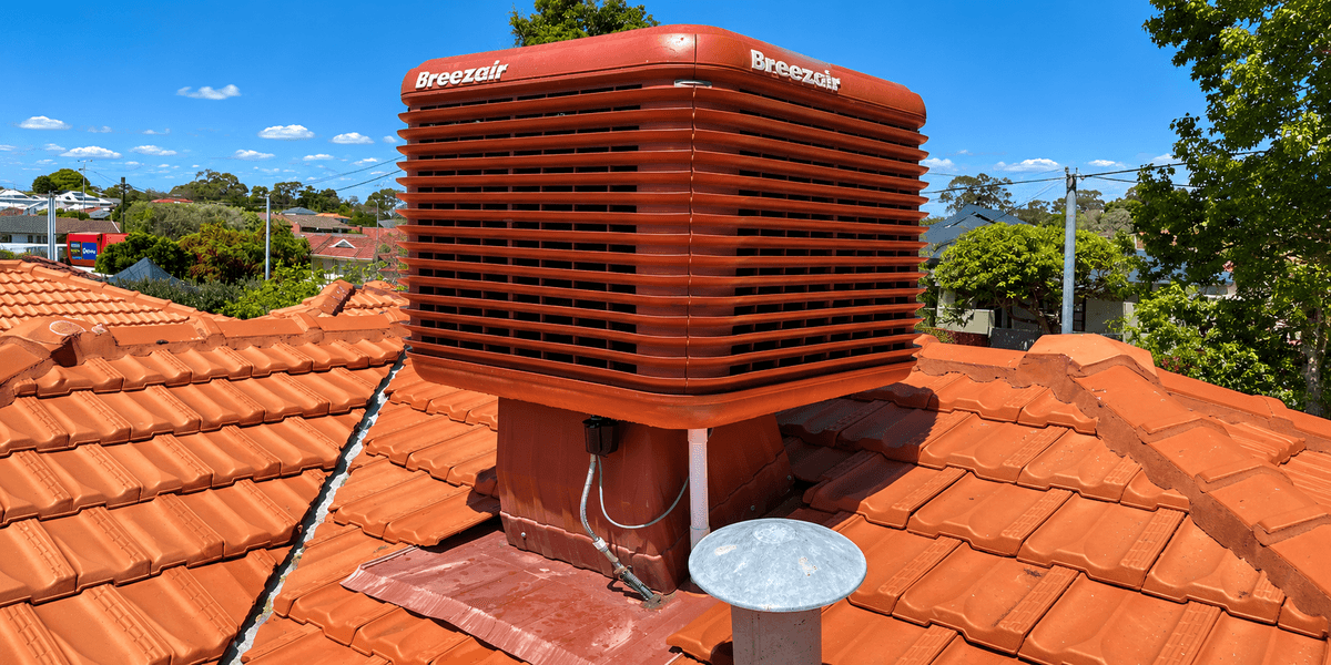 Breezair evaporative cooler on a terracotta tiled rooftop under a clear blue sky