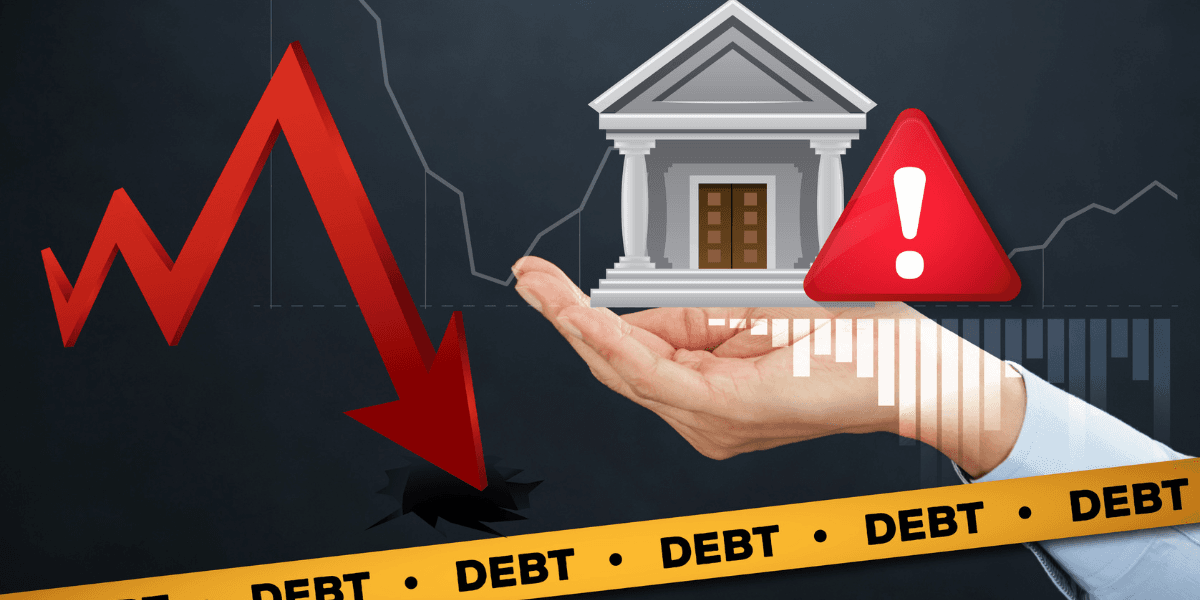 A hand holds a bank icon above a downward red arrow and debt warning signs