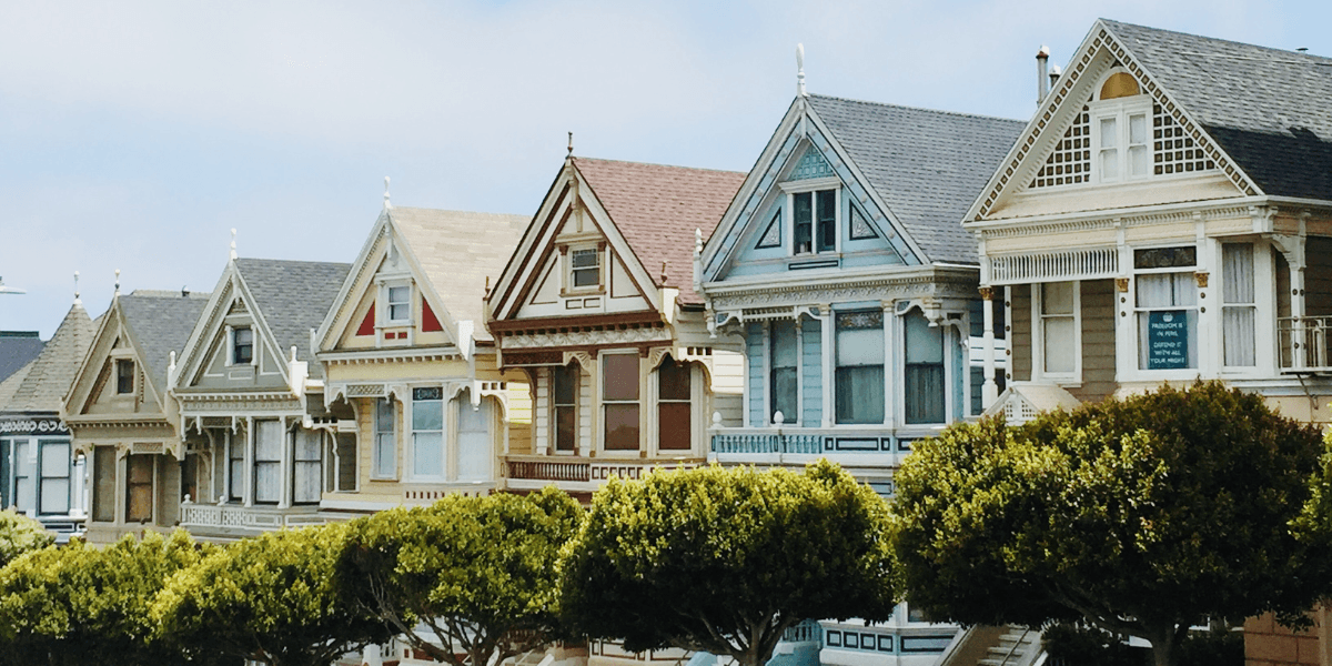 Colorful Victorian-style houses lined up with lush green trees in the foreground