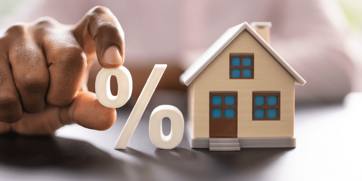 Person holding a percentage symbol next to a miniature house model