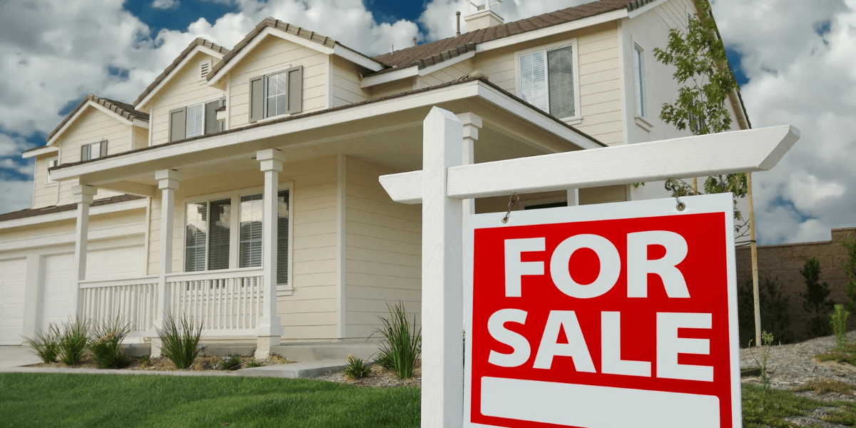 White house with a "For Sale" sign in front and blue sky background