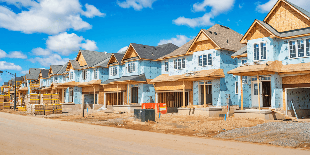 Newly constructed blue houses with wooden frames along a gravel road under a clear sky
