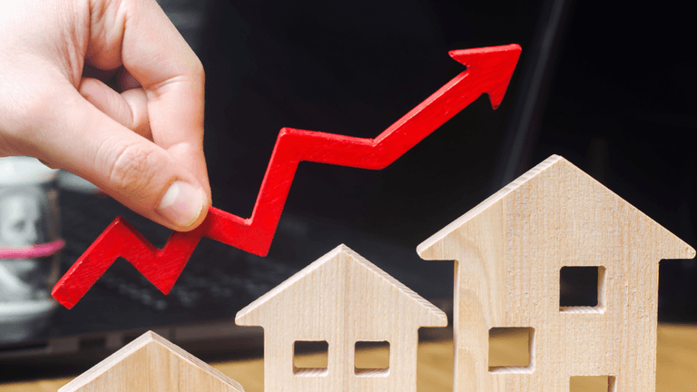 Hand placing a red upward arrow above wooden house models, illustrating rising housing inventory and market trends.
