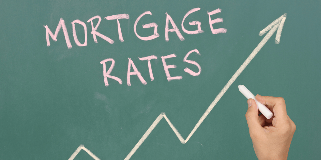 Hand drawing an upward trend beneath the words "Mortgage Rates" on a chalkboard.