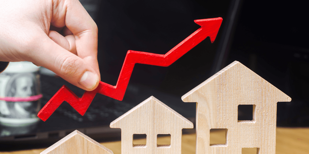 Hand placing a red upward arrow above wooden house models, illustrating rising housing inventory and market trends.