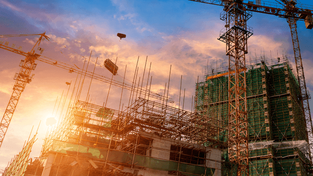 Construction site at sunset with cranes and scaffolding against a colorful sky