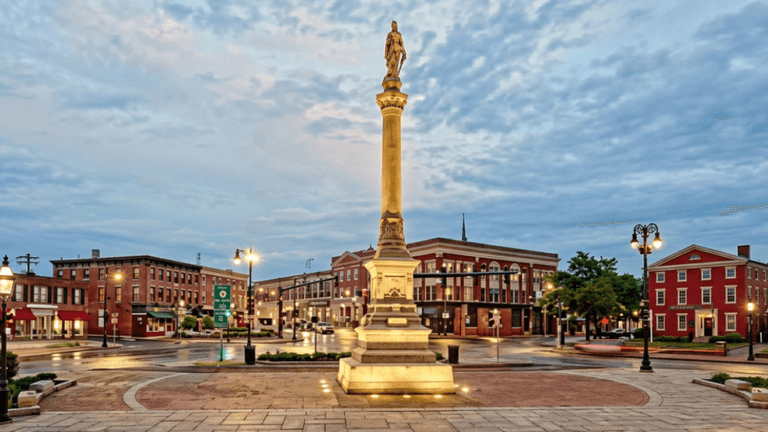 A town square featuring a statue on a pedestal surrounded by historic buildings.