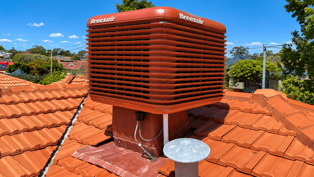 Breezair evaporative cooler on a terracotta tiled rooftop under a clear blue sky