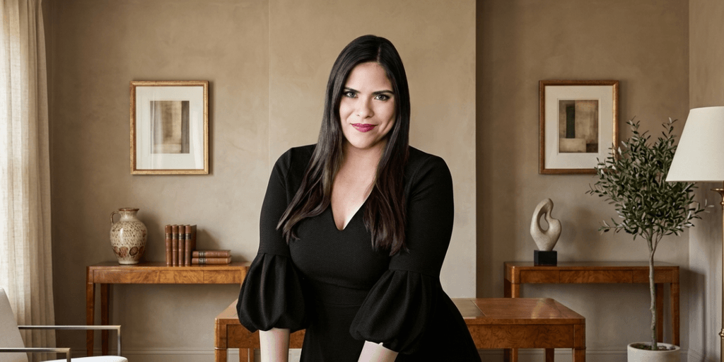 A woman with long dark hair stands confidently in a stylish, modern interior