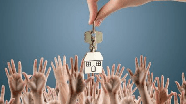 A hand holds house key above multiple reaching hands in a crowd.
