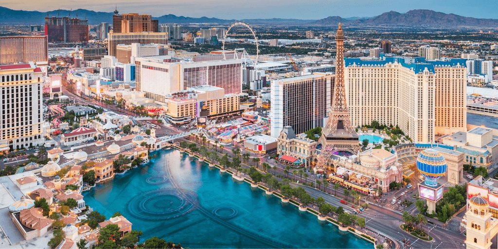 Aerial view of the Las Vegas Strip with hotels, fountains, and mountains in background