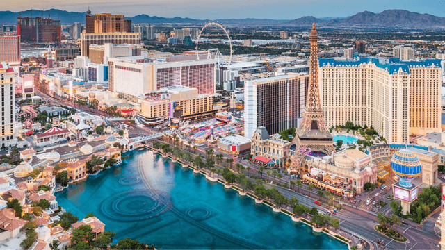 Aerial view of the Las Vegas Strip with hotels, fountains, and mountains in background