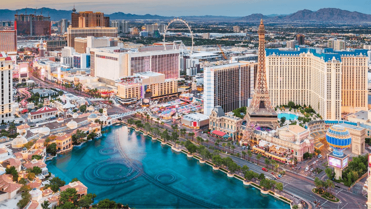 Aerial view of the Las Vegas Strip with hotels, fountains, and mountains in background