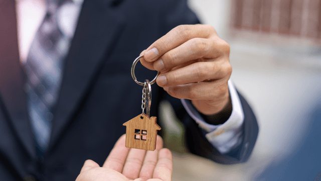 Person handing over a wooden house keychain to another person's hand