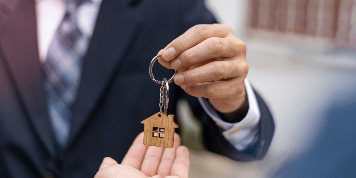 Person handing over a wooden house keychain to another person's hand