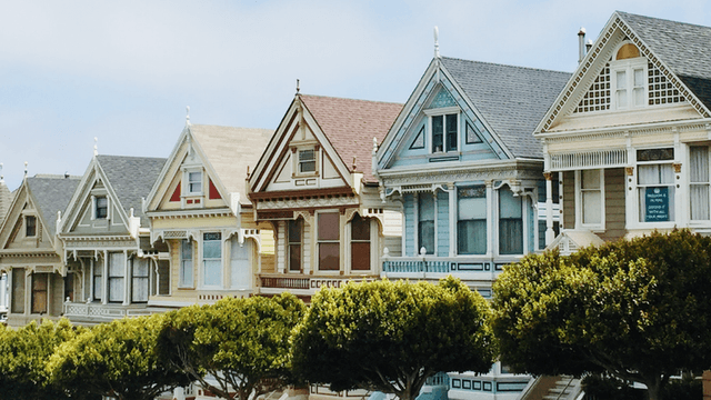 Colorful Victorian-style houses lined up with lush green trees in the foreground