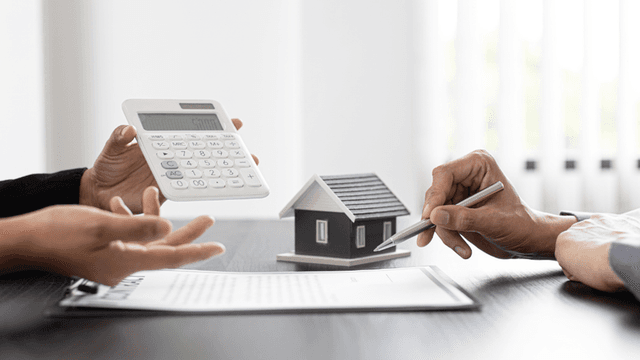 Hands discussing a house model with a calculator and contract on the table