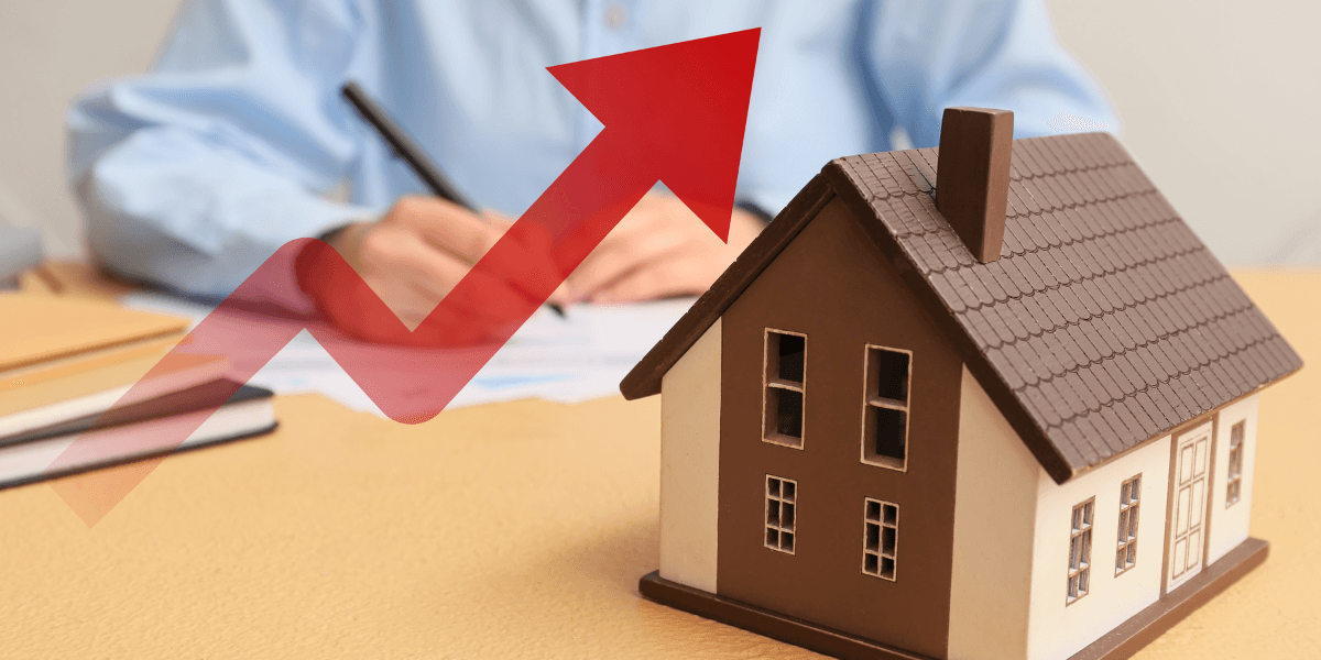 A miniature house model with an upward trend arrow and a person writing in the background