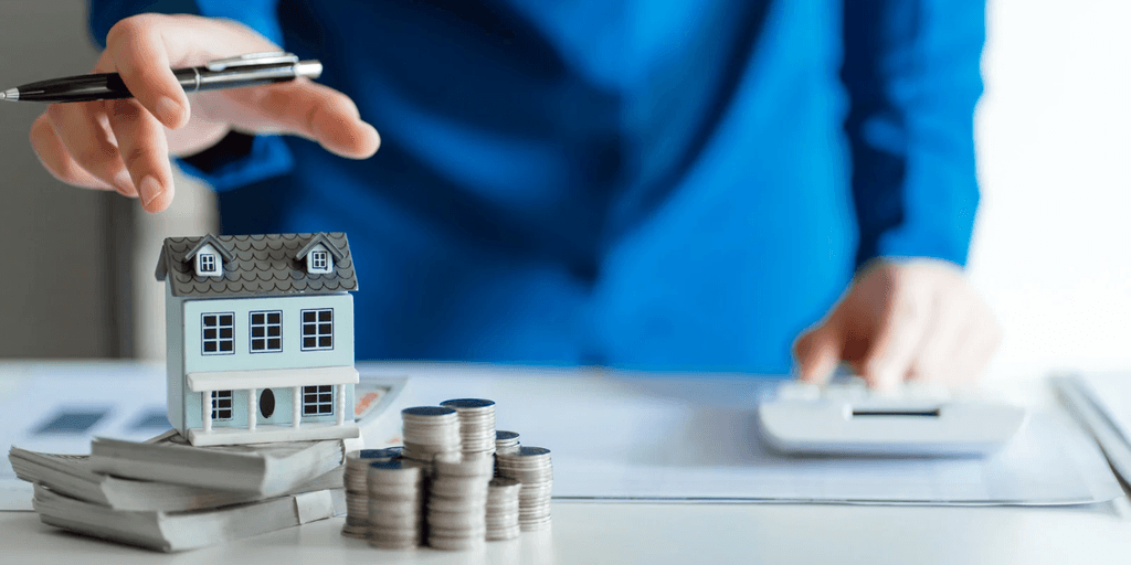 Person in a blue suit analyzing real estate investment with model house and coins