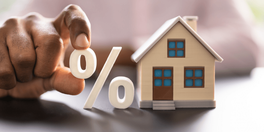 Person holding a percentage symbol next to a miniature house model