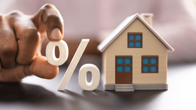 Person holding a percentage symbol next to a miniature house model