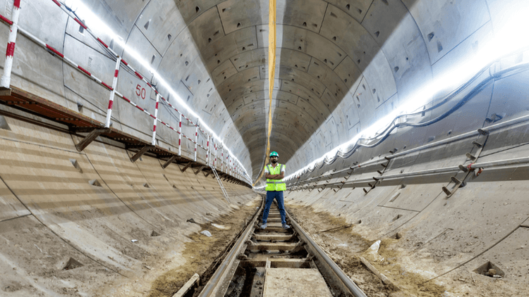 Worker in safety gear stands on tracks inside a tunnel under construction