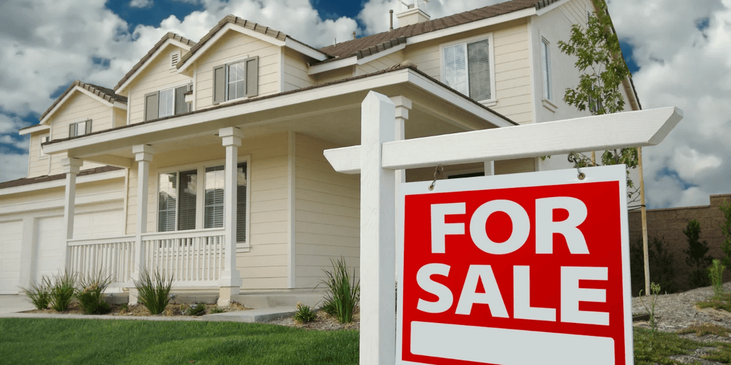 White house with a "For Sale" sign in front and blue sky background