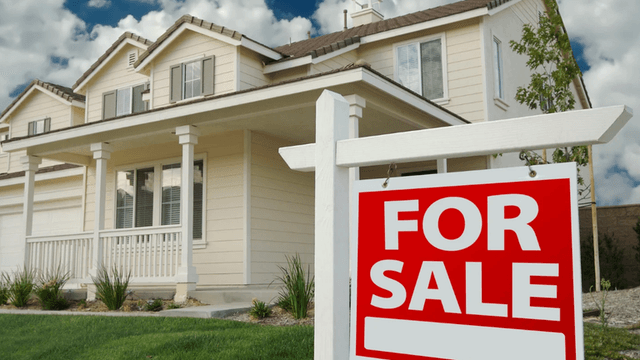 White house with a "For Sale" sign in front and blue sky background