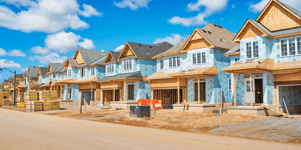 Newly constructed blue houses with wooden frames along a gravel road under a clear sky