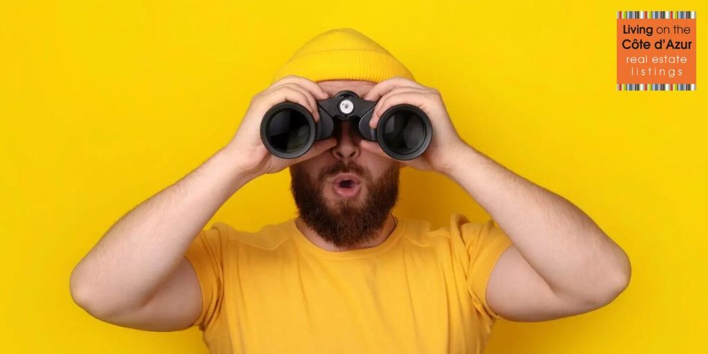 Man in yellow shirt and beanie looking through binoculars, symbolizing guided property search on the French Riviera.