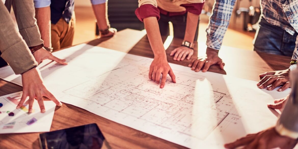 Multiple hands pointing at a blueprint during a collaborative meeting, likely related to a home remodeling project.