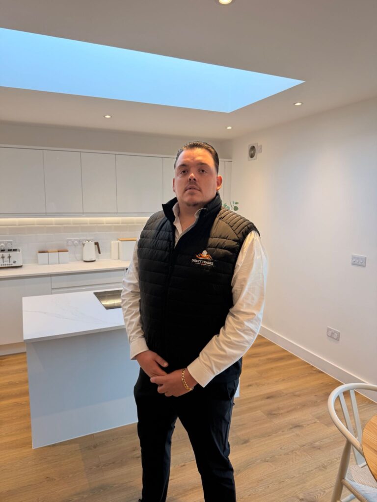 Rachid Amary standing in a newly renovated modern white kitchen wearing a Direct Trades branded vest.