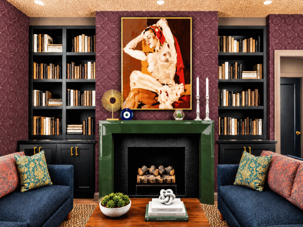 Living room with built-in bookshelves, green fireplace, colorful artwork, and blue sofas designed by Adrienne Morgan Interior Design.
